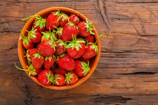 Fraises mûres dans une plaque d'argile sur une table en bois.