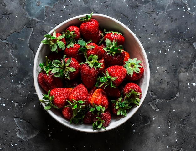 Fraises mûres fraîches dans un bol sur une vue de dessus de fond sombre