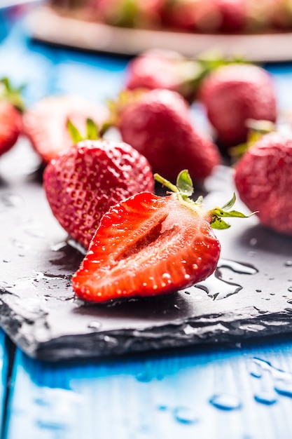 Fraises mûres fraîches lavées à l'eau sur table bleue.