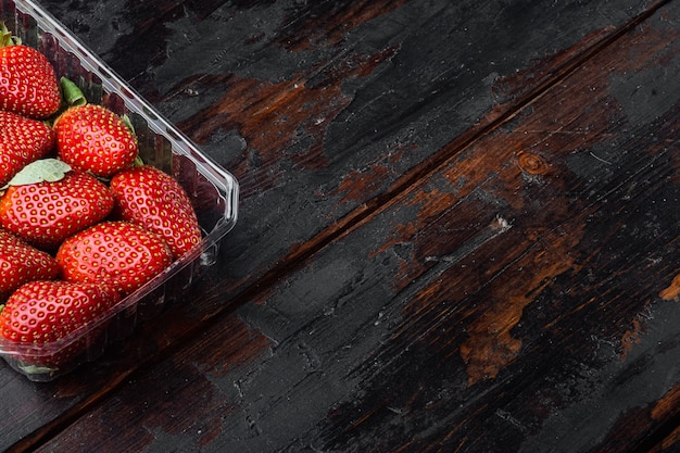 Fraises mûres rouges dans un bac en plastique transparent, sur la vieille table en bois sombre