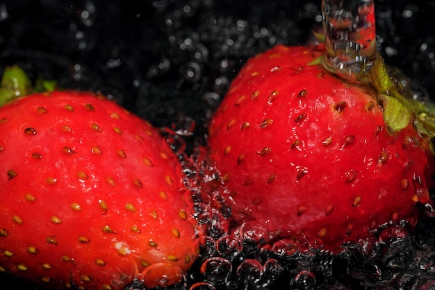Les fraises mûres rouges sont lavées dans de l'eau propre macrophotographie en gros plan sur fond noir