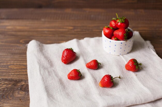 Fraises mûres sucrées dans le bol blanc qui se dresse sur le torchon. Fond en bois