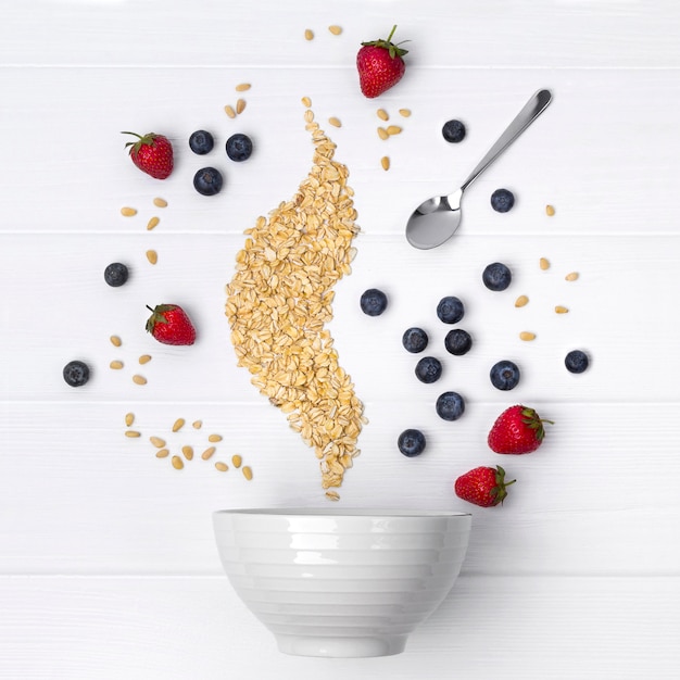 Fraises, myrtilles, pignons de pin et flocons d&#39;avoine coulent dans un bol en céramique pour la cuisson de muesli ou de granola fait maison