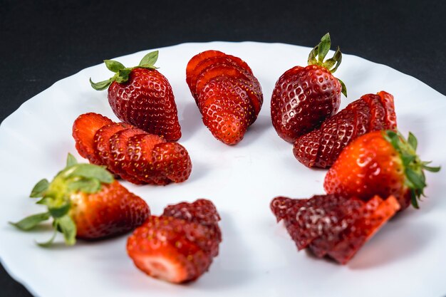 Fraises naturelles coupées en tranches sur une plaque blanche sur fond noir