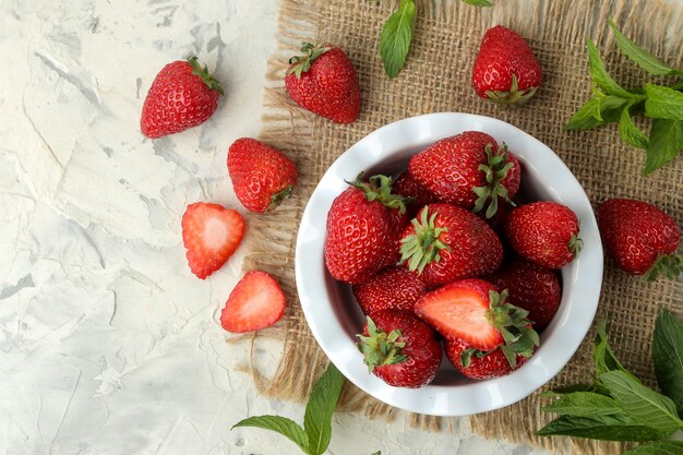 Fraises rouges dans un bol en céramique sur une table en béton clair et tissu, vue de dessus