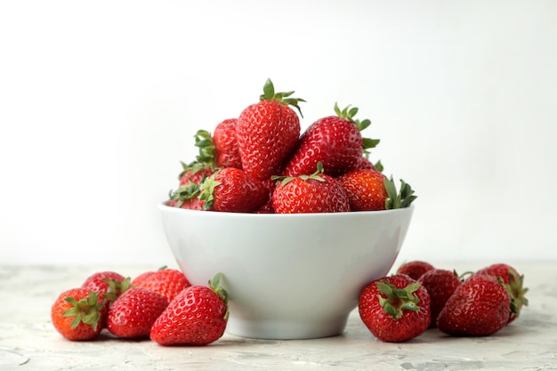 Fraises rouges dans un bol en céramique sur une table en béton clair.