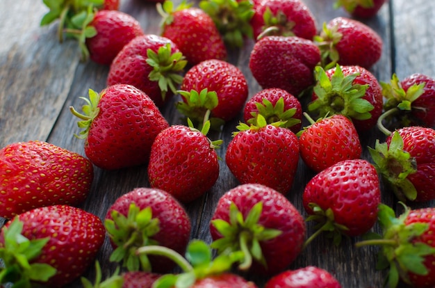 Fraises rouges mûres controlam lumière vive sur la vieille table en bois