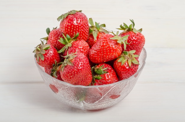 Fraises rouges mûres dans un bol sur une table en bois blanc, vue latérale