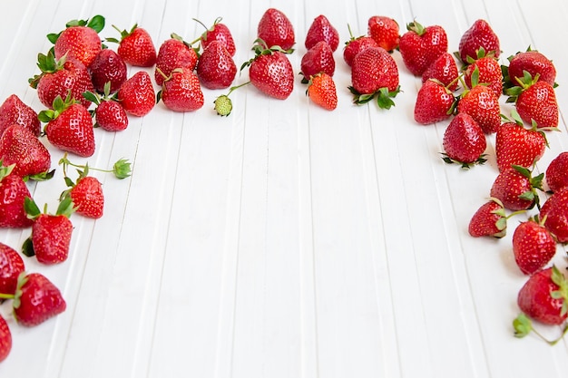 Fraises rouges mûres éparpillées sur un fond de table en bois blanc avec des fraises