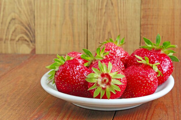 fraises rouges mûres sur la plaque blanche sur le fond brun