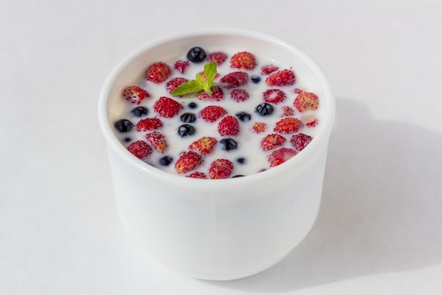 Fraises sauvages fraîches avec du lait dans une tasse blanche.