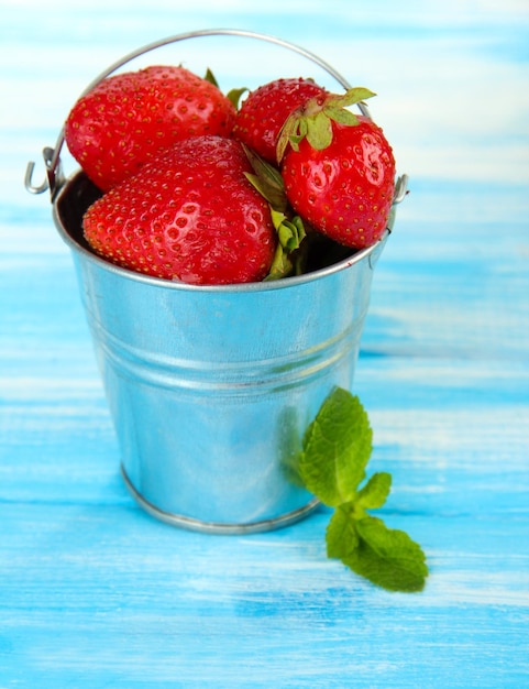 Fraises sucrées mûres dans un seau en métal sur une table en bois bleue