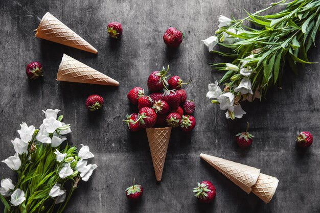 Fraises en tasses sur une surface gris foncé avec des gaufres et des fleurs blanches. Nourriture saine, fruits