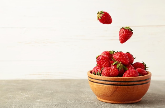 Les fraises tombent dans un bol en bois sur fond gris Espace pour le texte