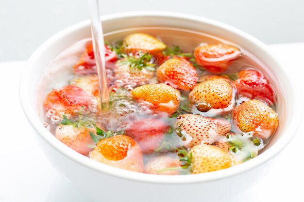 Fraises trempées dans l&#39;eau. Laver les fruits frais sur blanc.