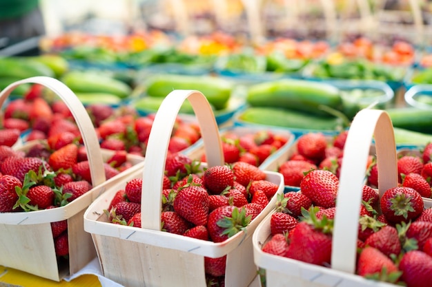 Fraises à vendre sur le marché des légumes Fraise juteuse crue dans un panier en bois debout sur l'affichage du marché avec d'autres fruits et baies sur fond