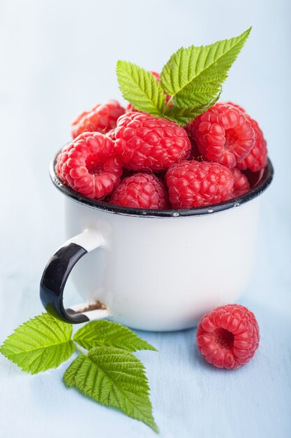 Framboise fraîche dans une tasse en émail sur fond bleu