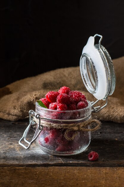 Framboise en pot de verre sur un fond en bois sombre. Fond de framboise. Nourriture saine conce