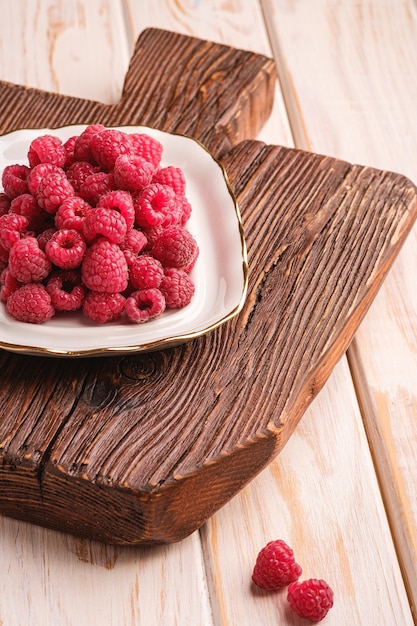 Framboises en assiette sur une vieille planche à découper en teck, tas sain de baies d'été sur une surface en bois, vue d'angle