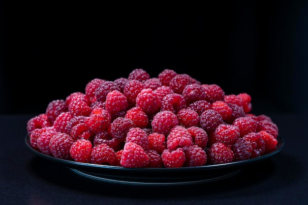 Framboises biologiques fraîches dans une assiette sur fond noir