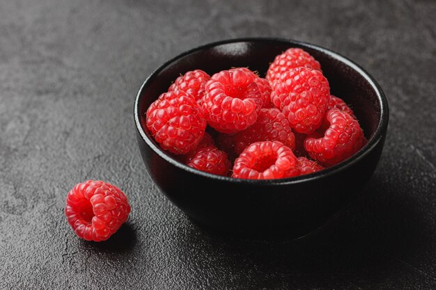 Des framboises dans un bol sur un fond sombre.