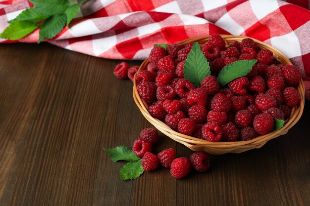 Framboises dans un bol en osier et un torchon sur une table en bois.