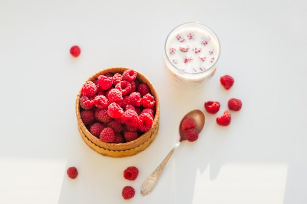 Framboises dans un bol avec une tasse de lait sur fond blanc. Vue de dessus