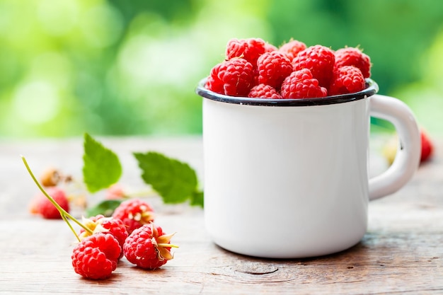 Framboises fraîches dans une tasse émaillée blanche sur table à l'extérieur