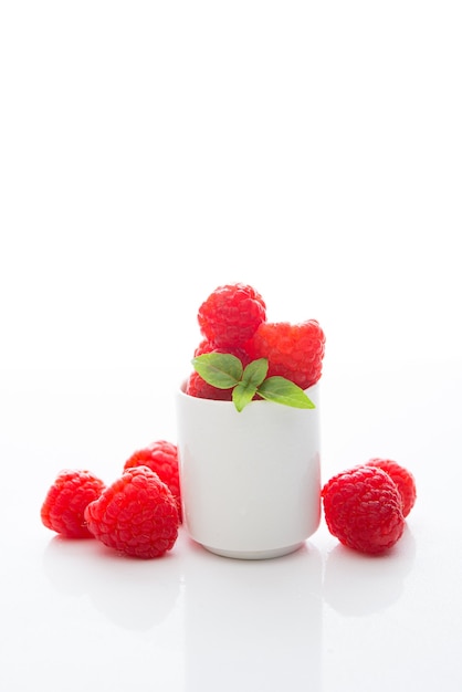 Framboises fraîches du jardin dans un verre blanc sur blanc