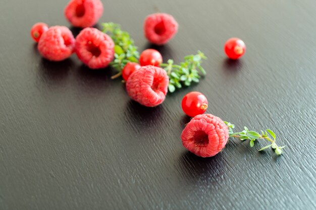 Framboises fraîches et groseilles dispersées sur un fond noir.