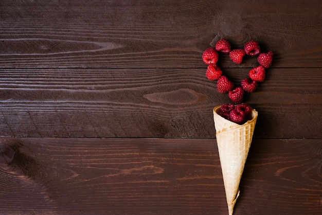 Framboises fraîches de jardin fait maison dans un cornet de crème glacée à la gaufre et un cœur de framboise sur un fond marron