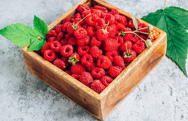 Framboises fraîches sélectionnées sur une boîte en bois sur fond de béton.