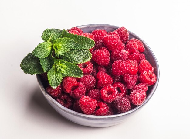 Framboises juteuses fraîches dans un bol sur fond blanc