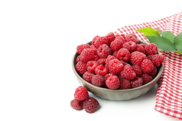 Framboises juteuses rouges dans un bol et un torchon, isolés sur fond blanc.