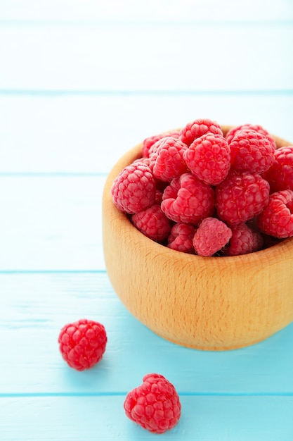 Framboises mûres dans un bol en bois sur fond bleu