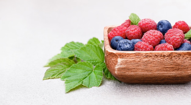 Framboises et myrtilles dans une assiette en bois sur fond de béton