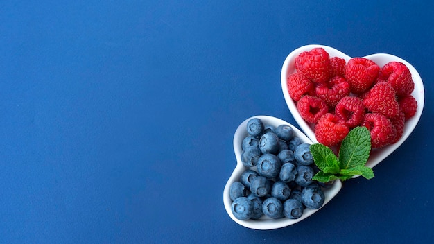 Des framboises et des myrtilles fraîches et belles sont disposées sur des assiettes en forme de coeurs