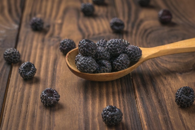 Framboises noires dans une cuillère en bois et sur la table