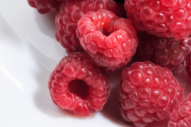 Framboises rouges douces mûres fraîches sur plaque blanche close up macrophotographie