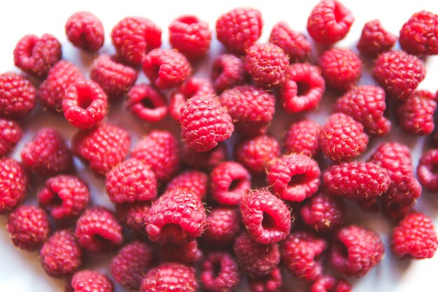 Framboises sucrées crues mûres isolées sur un tableau blanc avec des ombres