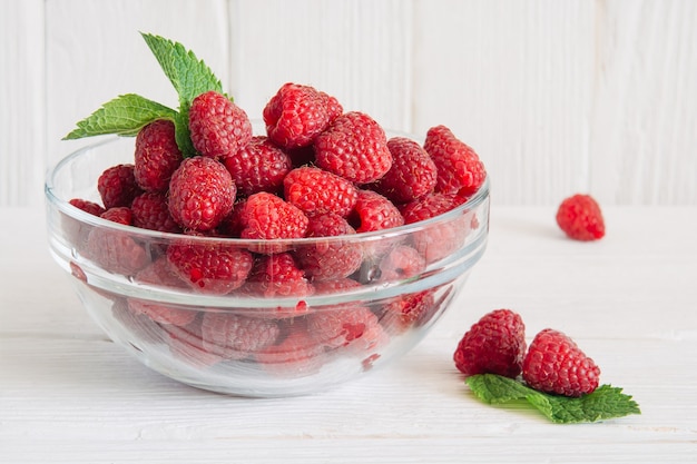 Framboises sucrées mûres dans un bol sur une table en bois décorée de menthe