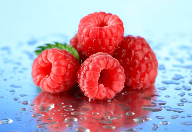 Framboises sucrées mûres avec des gouttes, sur fond bleu