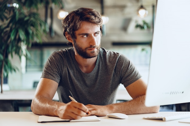 Freelance homme barbu à l'aide d'un ordinateur dans un lieu de coworking moderne