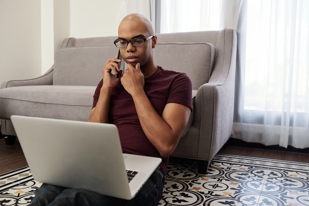 Freelance Sérieux Se Frottant Le Menton En Parlant Au Téléphone Avec Le Client Et En Lisant Le Contrat Sur L'écran Du Portable