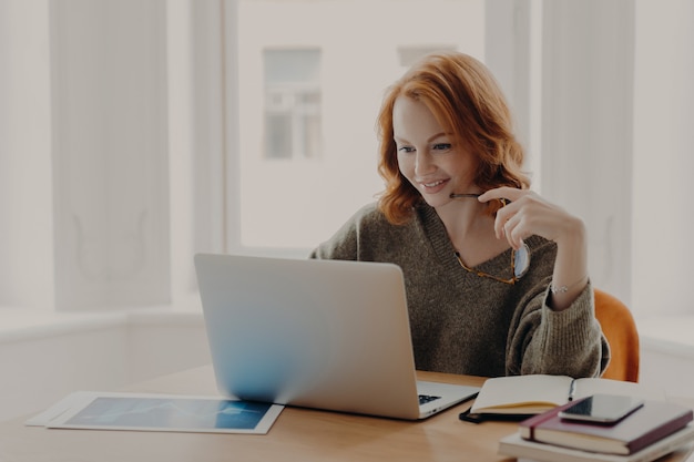 Freelancer aux cheveux roux se trouve au bureau concentré dans un ordinateur portable