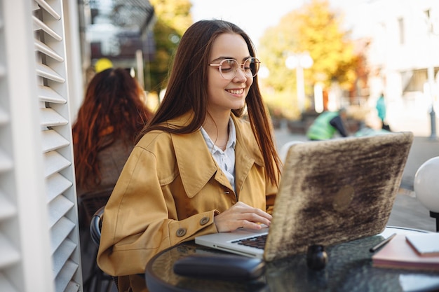 Freelancer féminin positif naviguant sur un ordinateur portable pendant le travail à distance sur un projet en ligne dans un café de rue