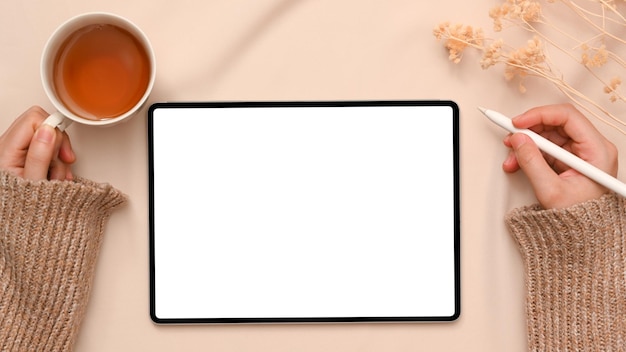 Freelancer féminin tenant une tasse de thé tout en utilisant une tablette numérique dans son espace de travail minimaliste