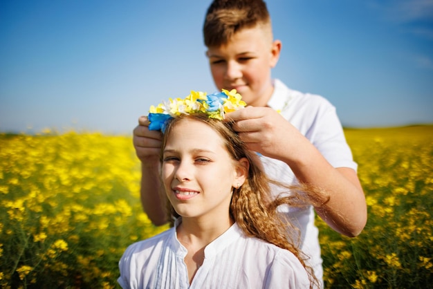 Un frère met une couronne ukrainienne de sa sœur dans un champ de colza sous un ciel dégagé