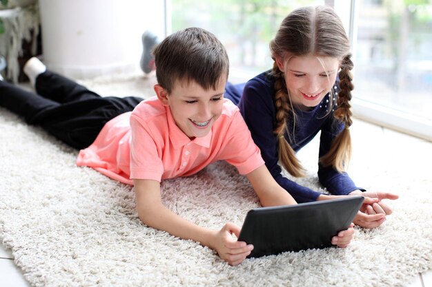Frère et sœur à l'aide d'une tablette numérique sur le sol à la maison