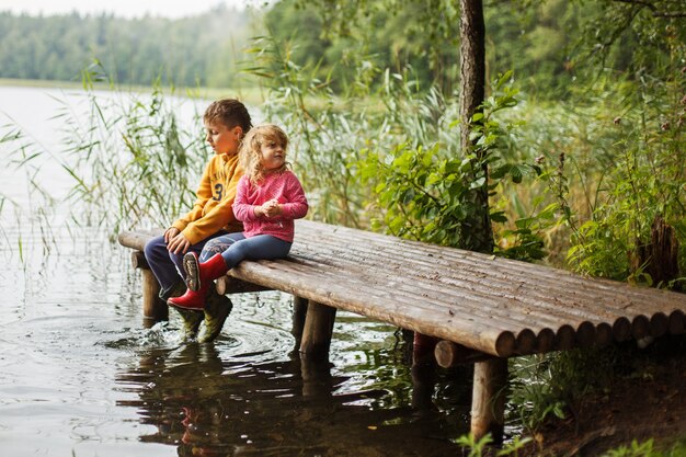 Frère et soeur assis sur la jetée de la rivière